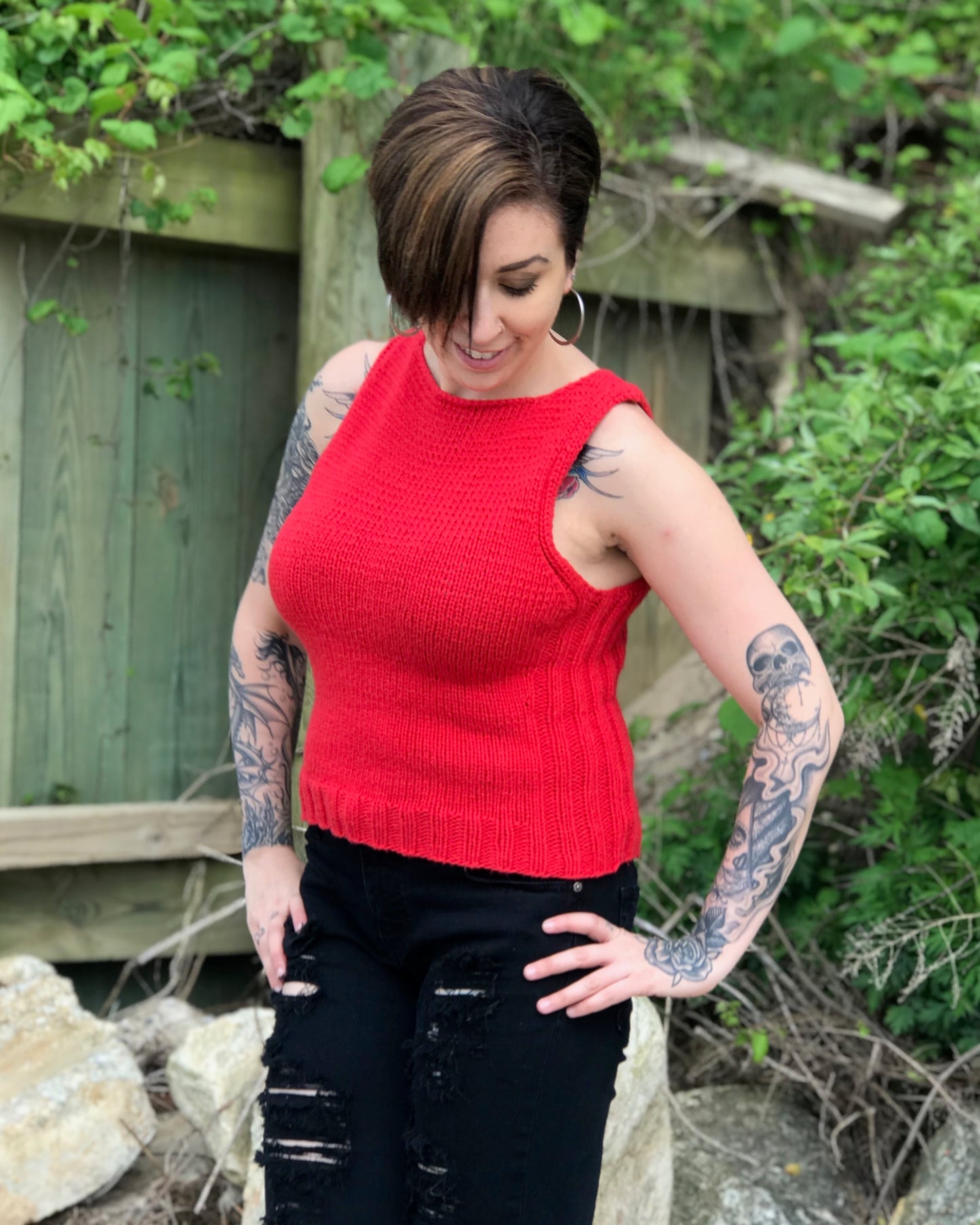 A person wearing a red Avalon tank top with a crew neckline, paired with black denim and standing outdoors.