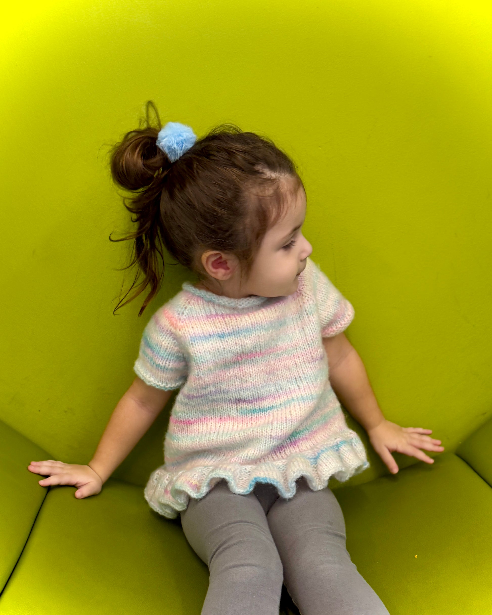Child wearing a colorful knitted dress sitting on a green couch.