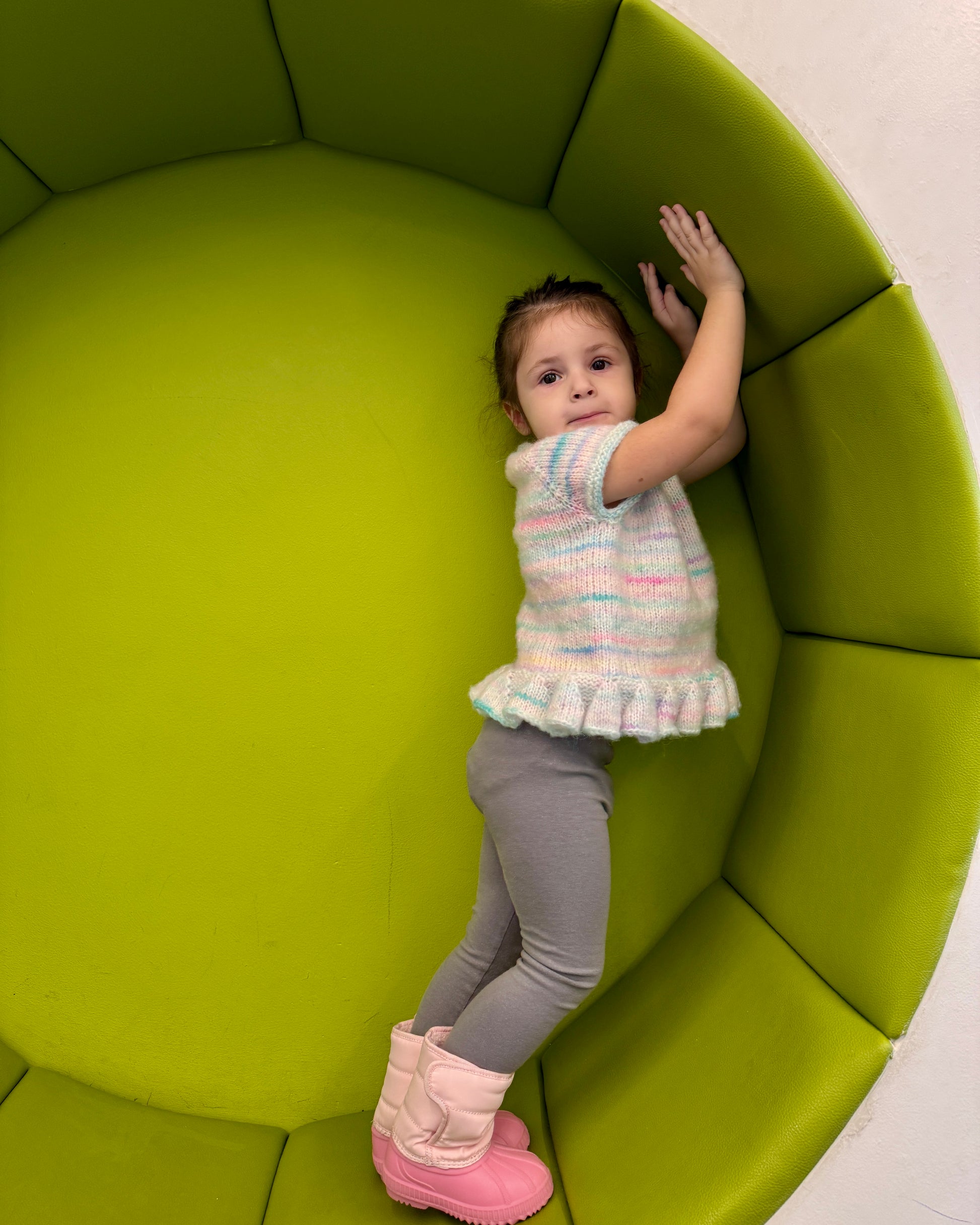 Child standing inside a green, modern chair with a plain background
