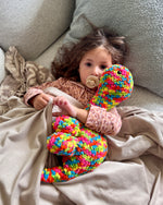 Load image into Gallery viewer, Child holding a colorful soft toy on a couch

