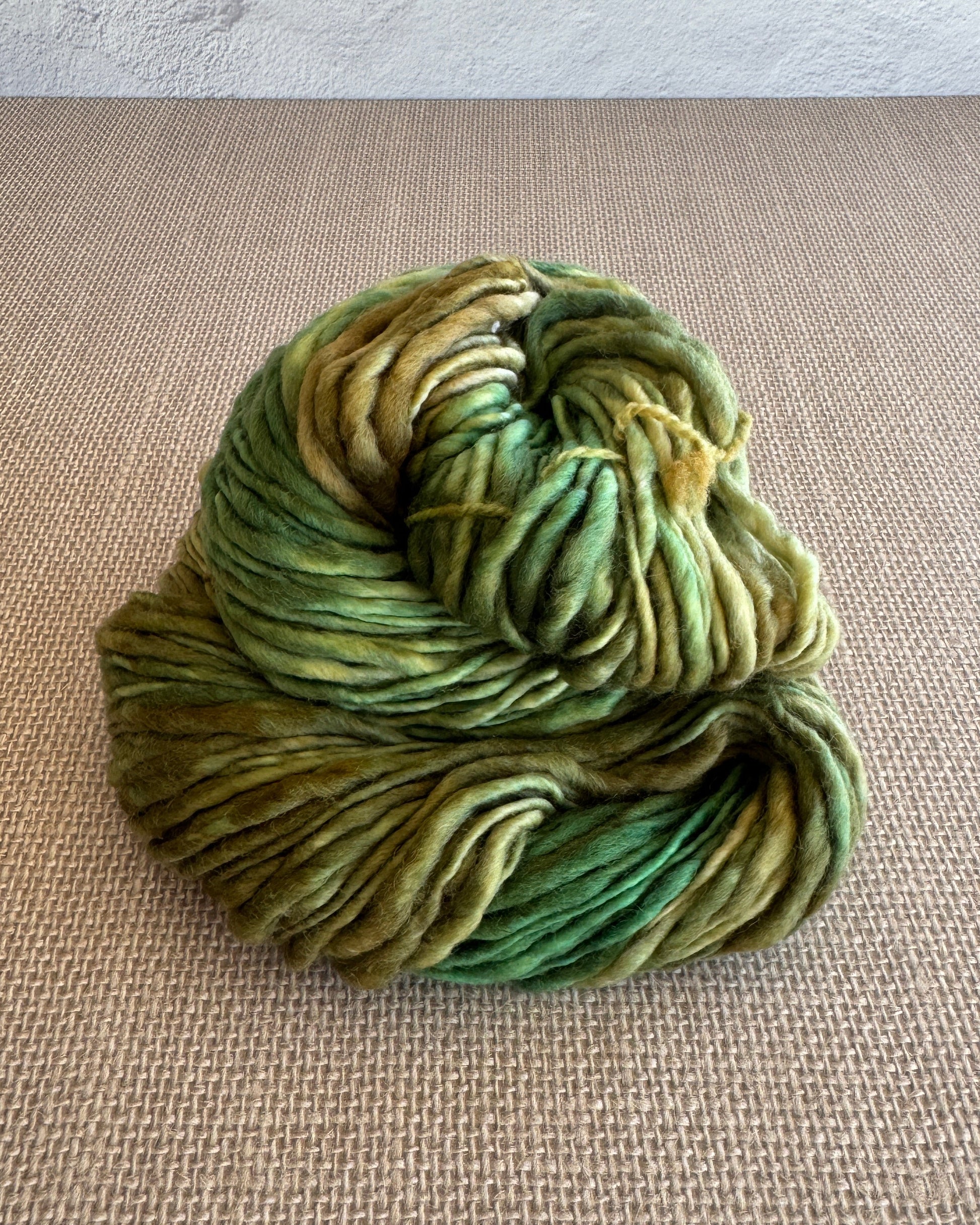 Green skein of yarn on a textured beige surface