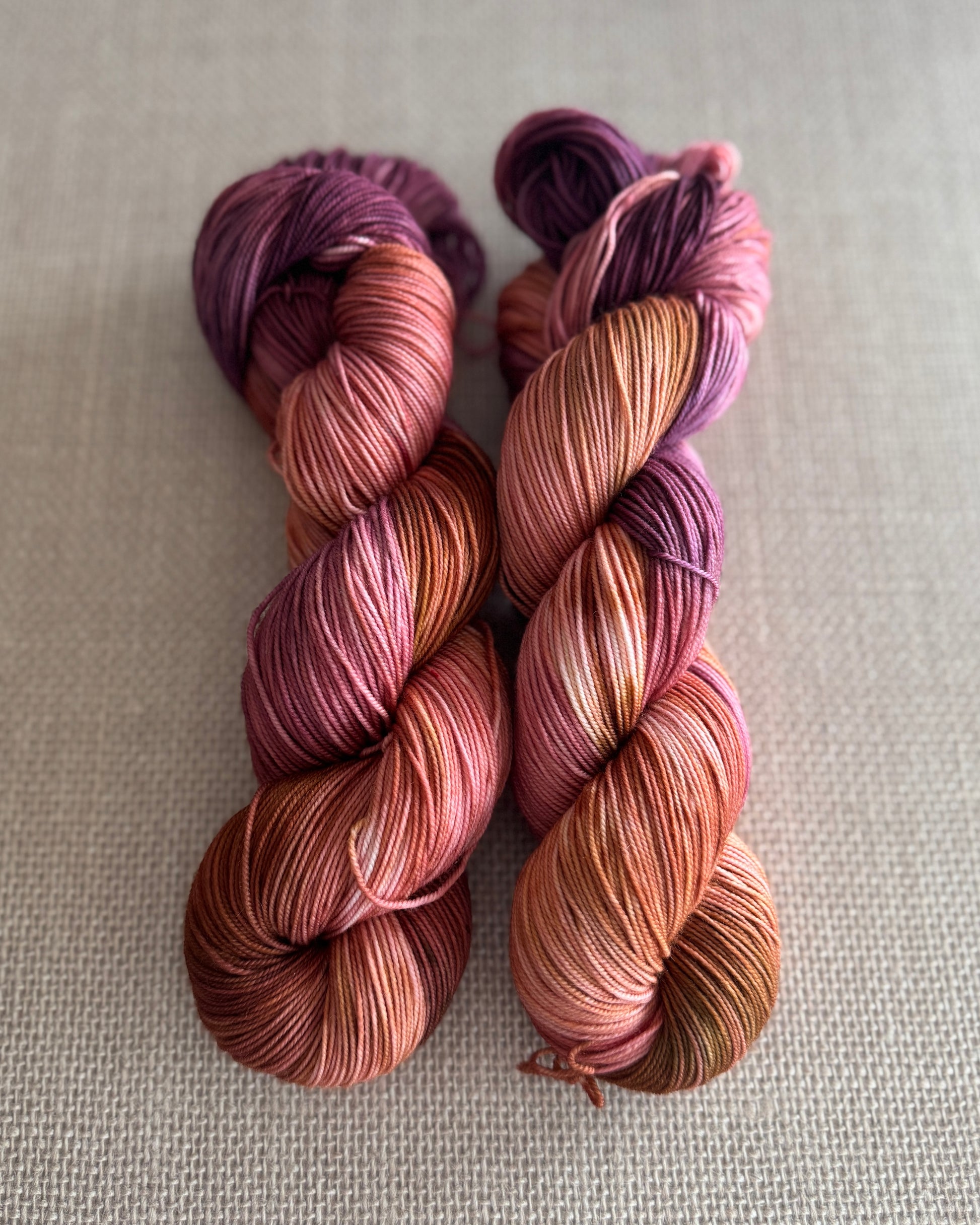 Two skeins of multicolored yarn on a textured beige background