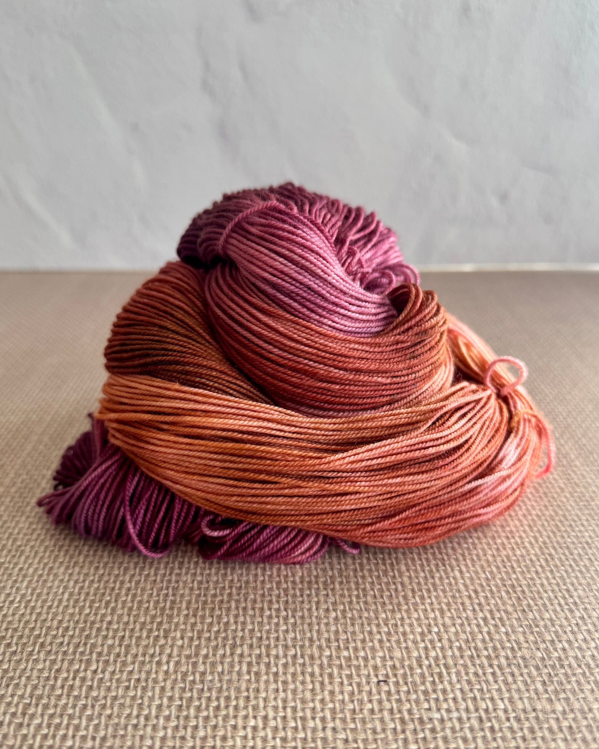 Skein of pink and purple yarn on a textured surface with a neutral background