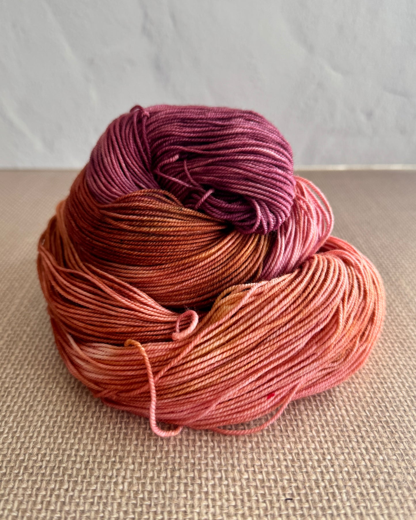 Hand dyed skein of yarn in purple, brown, and pink on a textured surface.