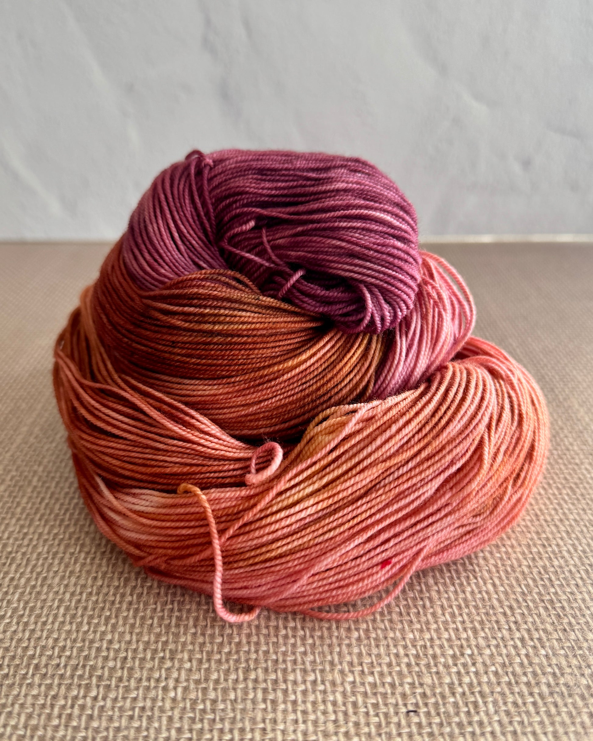 Hand dyed skein of yarn in purple, brown, and pink on a textured surface.