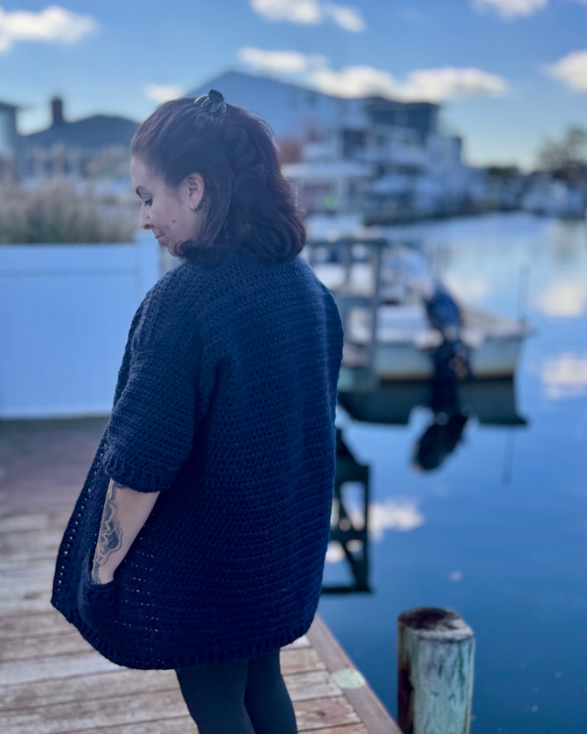 Crochet cardigan photographed outdoors by a coastal dock, casual handmade fashion.