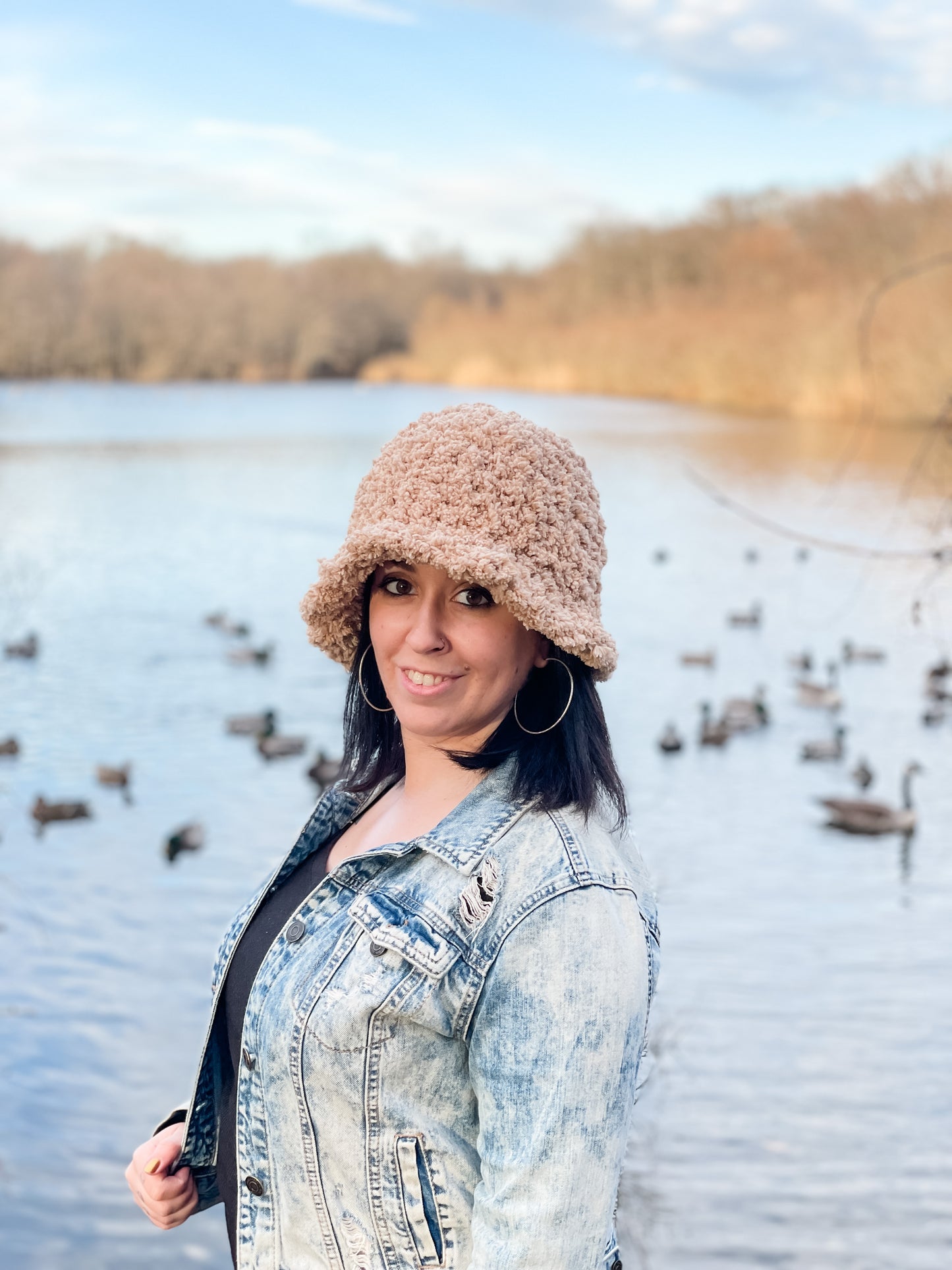 A person wearing a brown crochet bucket hat standing by a body of water, with a background of ducks.