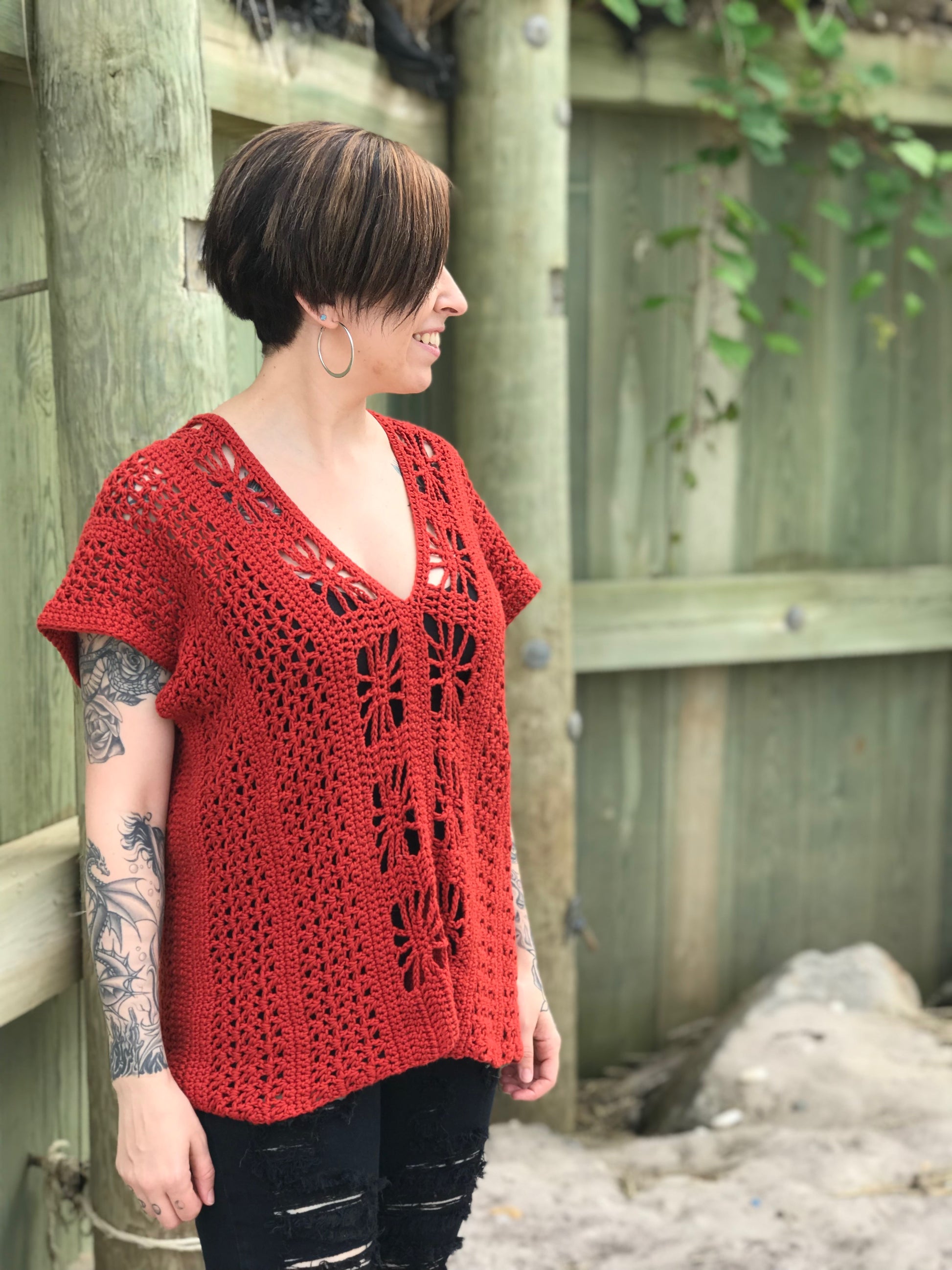 A person standing by a bulkhead, wearing a red crochet beach top with a V-neckline and sleeveless design, with a visible tattoo.