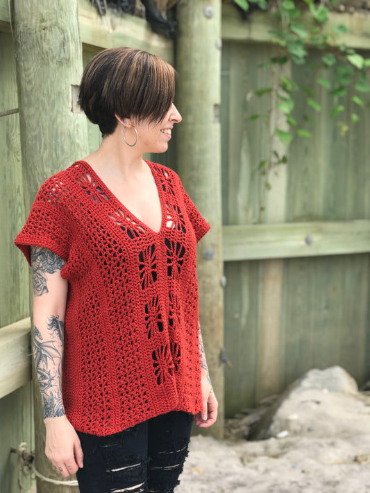 A person standing by a bulkhead, wearing a red crochet beach top with a V-neckline and sleeveless design, with a visible tattoo.